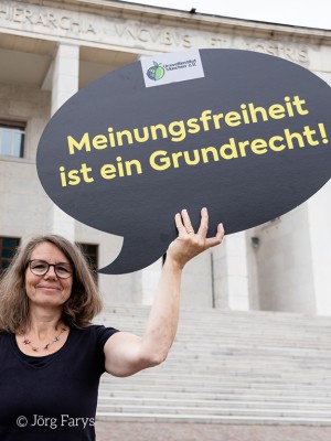 Eine Frau hält ein Schild mit der Aufschrift "Meinungsfreiheit ist ein Grundrecht"